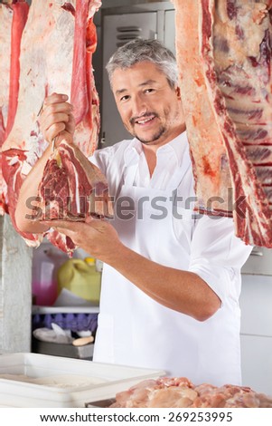 Portrait of confident male butcher holding raw meat with hook in shop