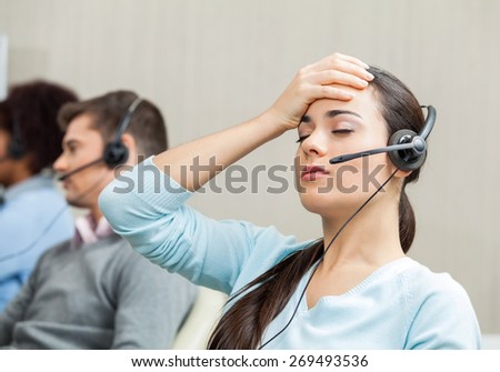 Tired female customer service agent with colleagues in background at call center
