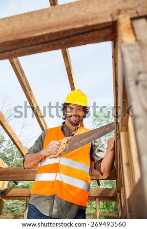 Low angle portrait of smiling worker cutting wood with handsaw at construction site