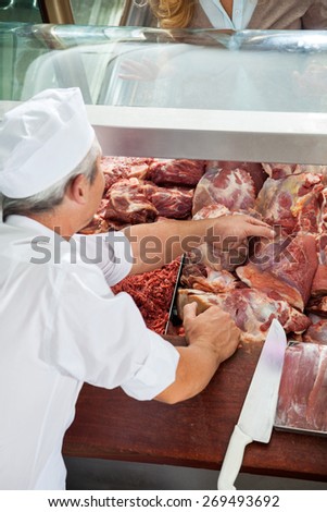 Male butcher arranging fresh meat in display counter at butchery