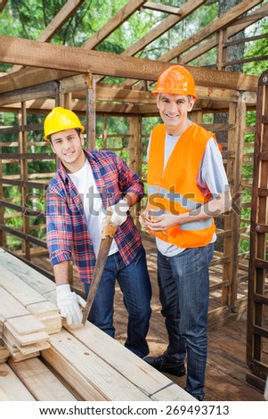 Portrait of happy male construction workers working together in timber cabin at site