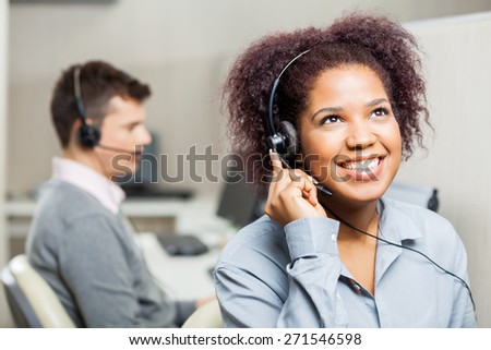 Happy female call center agent using headset with male colleague in office