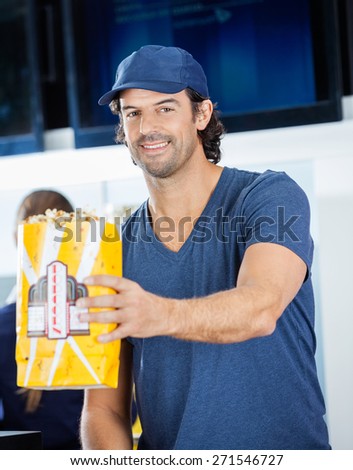 Portrait of smiling male worker offering popcorn paperbag at cinema concession stand