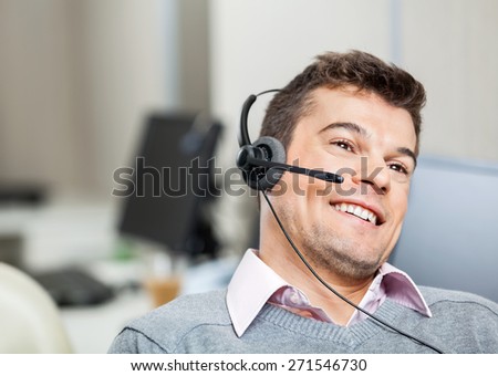 Smiling customer service representative wearing headset while looking away in office