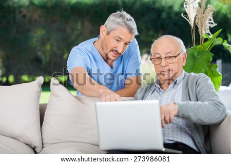 Male nurse explaining something on laptop to senior man at nursing home porch