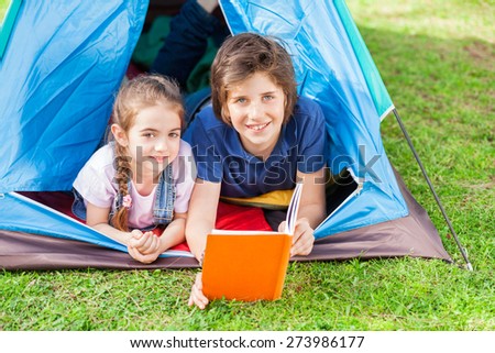 Portrait of smiling siblings reading book in tent at park