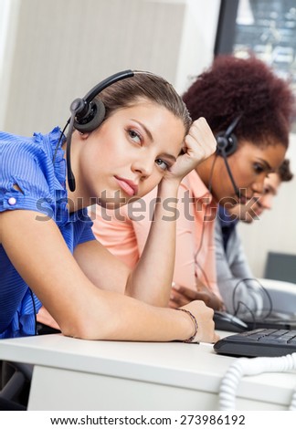 Tired female customer service representative looking away while colleagues working in office