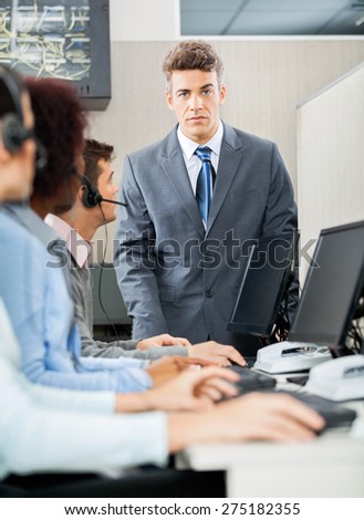 Portrait of confident manager standing in front of customer service representatives in office