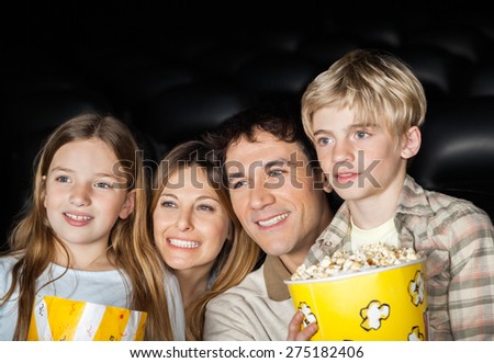 Happy family of four holding popcorn while watching film in movie theater