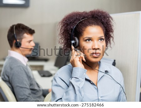 Serious female customer service representative using headset with male colleague in background at office