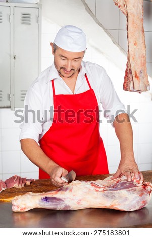 Mature male butcher cutting meat at counter in butchery
