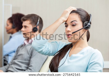 Tired female customer service representative with colleagues in background at call center
