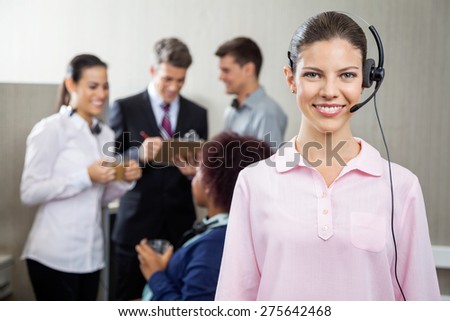 Portrait of beautiful customer service representative standing at office while team discussing in background