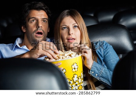 Shocked mid adult couple having popcorn while watching movie in cinema theater