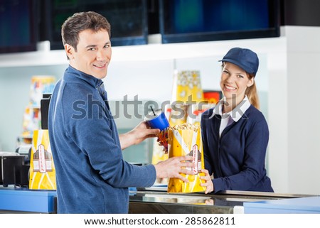 Portrait of smiling man buying popcorn and drink from seller at cinema concession stand