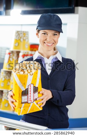 Portrait of confident female worker holding popcorn paperbag at cinema concession stand