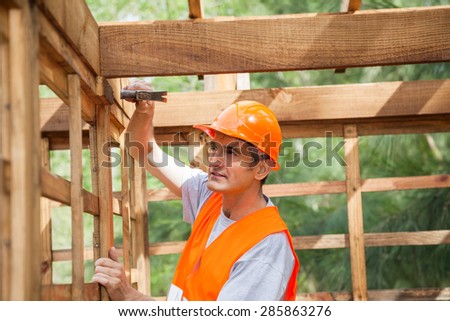 Male construction worker hammering nail on wooden cabin at site