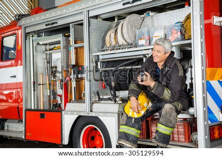 Happy fireman looking away while sitting in truck at fire station