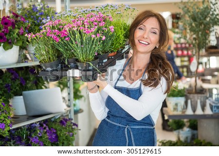 Portrait of smiling botanist carrying crate full of flower plants in store