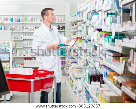 Mid adult male pharmacist counting stock while holding tablet computer at pharmacy
