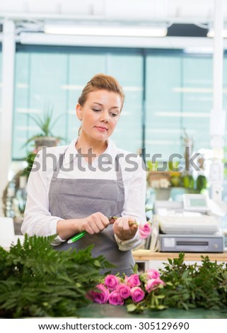 Female florist cutting stem on rose at counter in flower shop