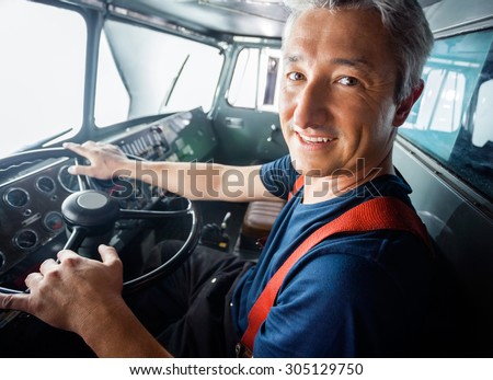 Portrait of happy mature firefighter driving firetruck