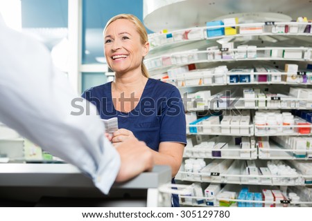Happy female chemist looking at male customer in pharmacy