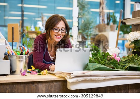 Happy mid adult female florist using laptop at counter in flower shop