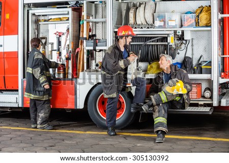 Full length of male firefighters discussing by truck at fire station