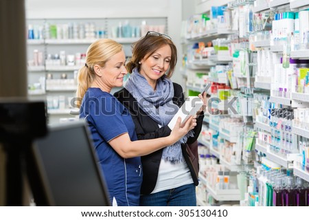 Smiling female chemist showing product to customer holding cell phone in pharmacy