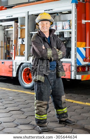 Portrait of happy fireman standing arms crossed against truck at fire station