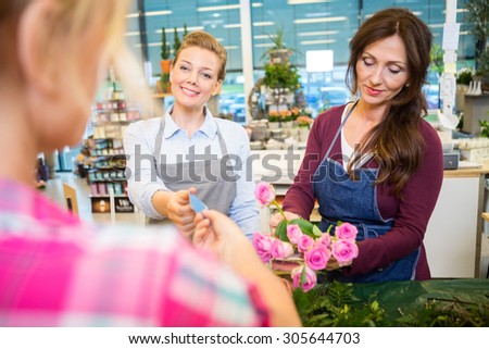 Happy florists selling rose bouquet to female customer in flower shop