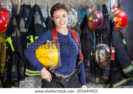 Portrait of happy firewoman holding helmet while standing at fire station