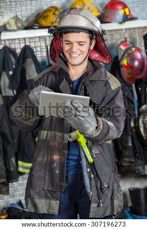 Happy fireman in uniform using digital tablet at fire station