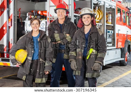 Portrait of happy firefighters standing together against truck at fire station