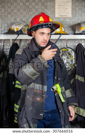 Young male firefighter looking away while using walkie talkie at fire station