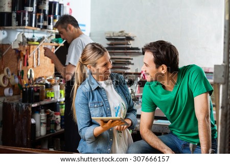 Happy female worker holding digital tablet while looking at male supervisor in paper factory