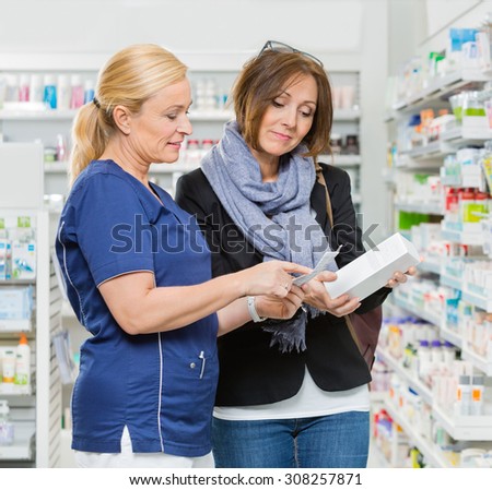 Mature female chemist explaining product details to customer in pharmacy
