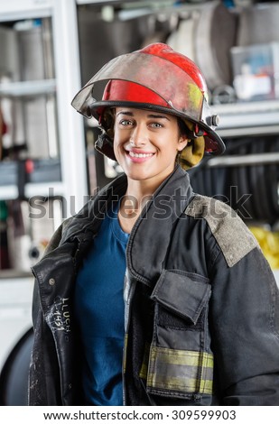 Portrait of happy female firefighter standing against firetruck at station
