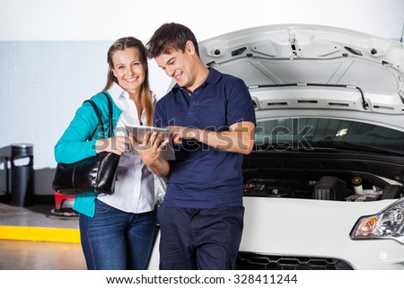 Portrait of happy female customer standing with mechanic using digital tablet by car in garage