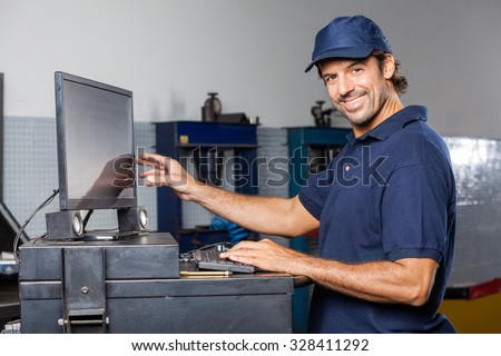 Portrait of happy male mechanic using computer in auto repair shop