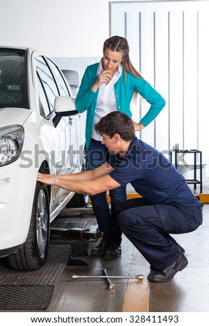 Female customer looking at mechanic changing car tire at garage