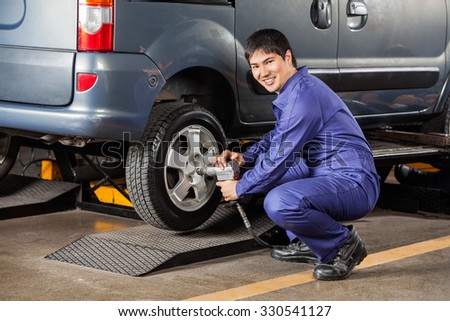 Side view portrait of happy mechanic fixing car tire pneumatic wrench at garage