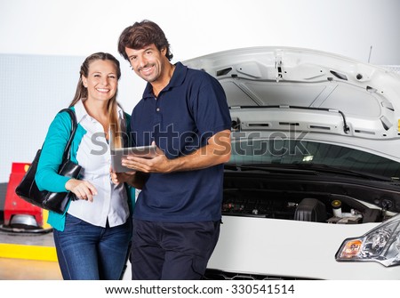 Portrait of happy female customer standing with technician holding digital tablet by car in garage
