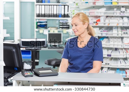 Female assistant looking at computer while sitting at cash counter in pharmacy