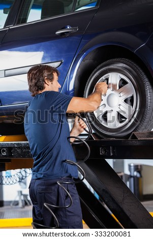 Rear view of male mechanic refilling car tire at auto repair shop