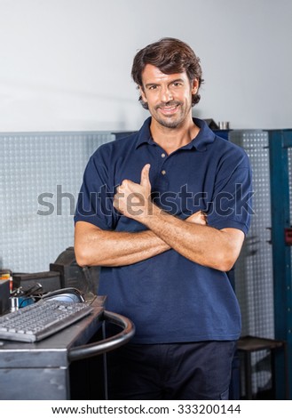 Portrait of happy male mechanic gesturing thumbsup while standing at auto repair shop