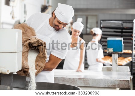 Smiling male baker pouring flour in kneading machine at bakery
