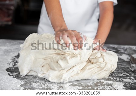 Closeup of female baker\'s hands kneading dough in bakery