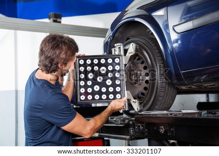 Male mechanic adjusting wheel alignment machine on car in garage